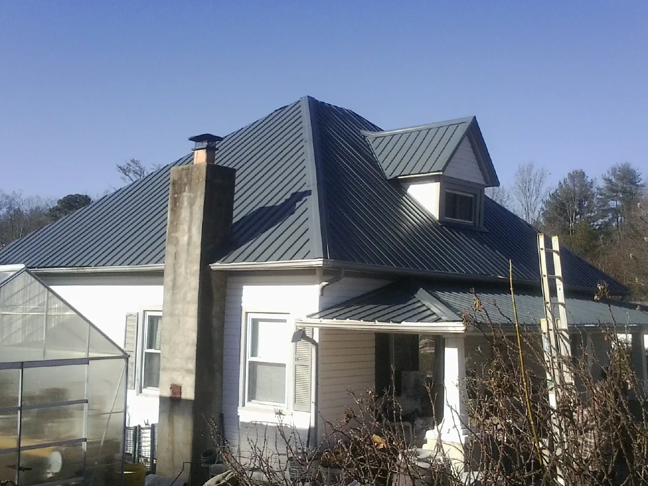 Dark blue standing seam metal roof on a white farmhouse with dormer — Slate & Tile Roof Repair by Roofing Brothers in Elm Mott