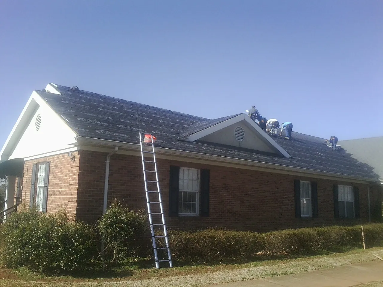 Crew tearing shingles off a brick ranch roof with a ladder set — Emergency Roof Repair work by our crew in Elm Mott