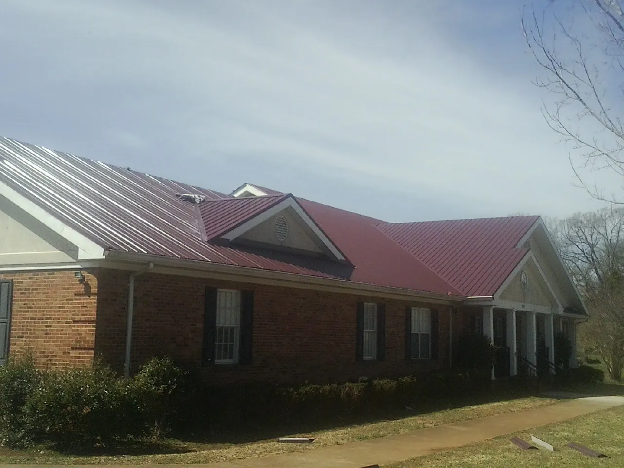 Red metal roof with gabled entries on a long brick building, from a Hail Damage Roof Repair job in Elm Mott