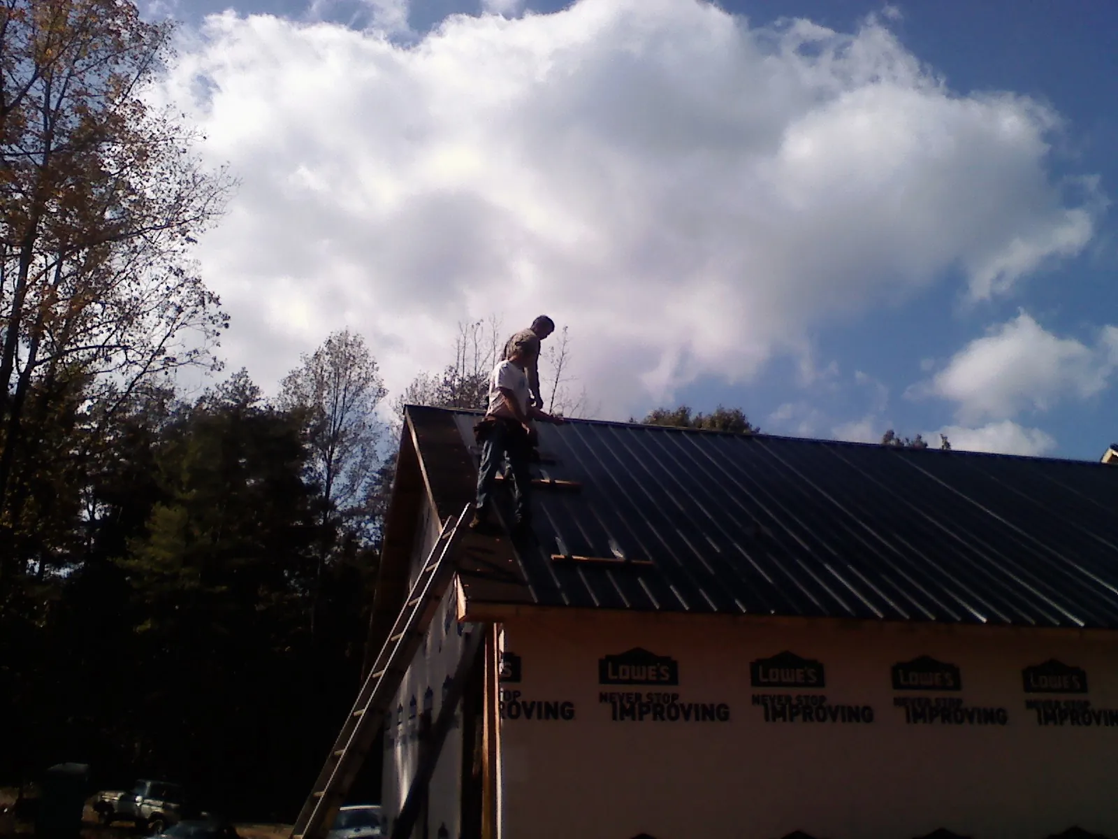 Roofer fastening dark metal panels high against a cloudy sky, from a Roof Inspection job in Elm Mott