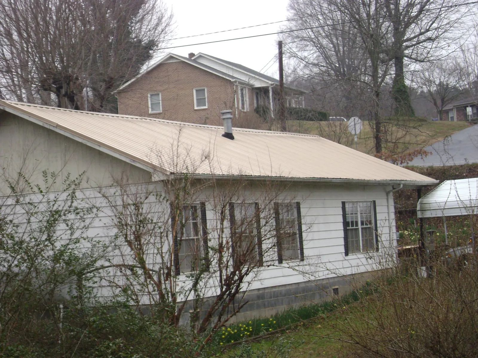 Tan metal roof on a white sided house set into a hillside — Commercial Roofing by Roofing Brothers in Elm Mott