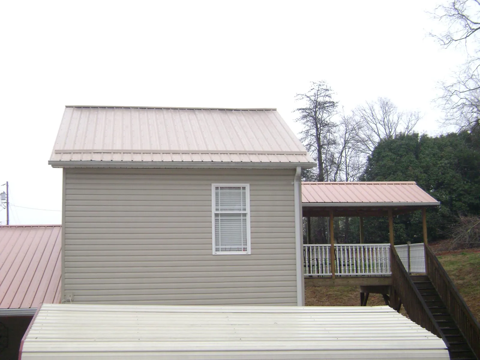 Tan metal roofs on a two story addition and attached porch, from a Roof Replacement job in Elm Mott